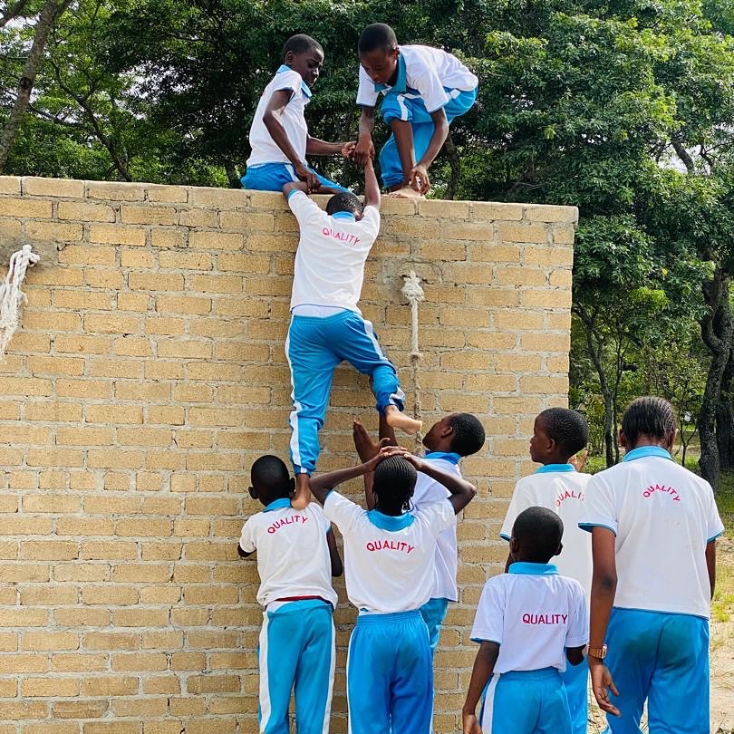 Quality students working as a team to scale a wall during outdoor leadership training